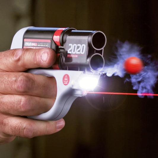 A hand squeezes the trigger of the HERO 2020. A PavaBall flies from the bottom barrel. A laser and bright light are lit on the device.