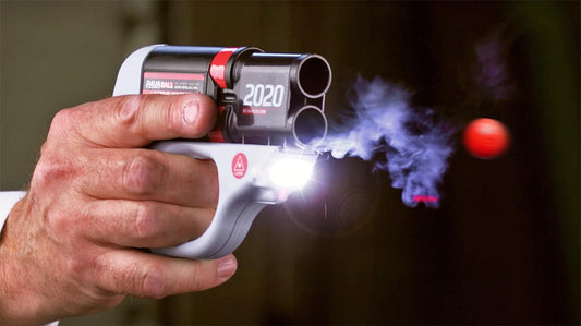 A hand squeezes the trigger, firing HERO® 2020. A projectile flies from the bottom barrel. A laser and bright light are lit on the device.