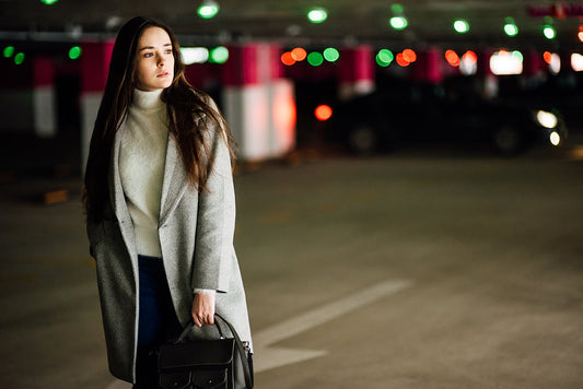 Beautiful young girl in a gray coat and with bag on car parking